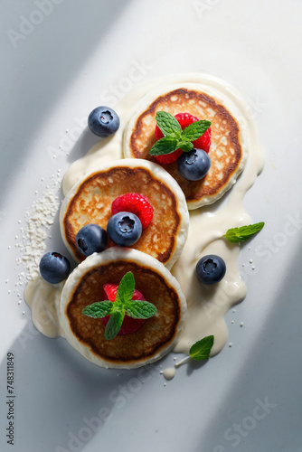 Pancakes with berries, mint leaves and delicate cream on a plate in bright daylight. 