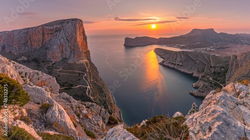 Breathtaking panorama of towering mountain cliffs beside a serene sea with a winding road, under the glow of a sunset