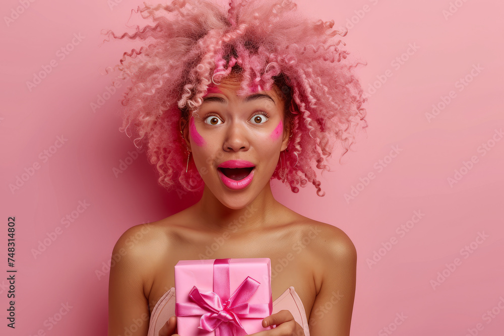 Portrait of a happy charismatic African American woman holding a gift box on a pink background. Holidays, celebrations and a feminine concept.