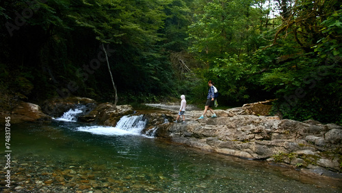 Woman and boy walking along natural pond with small waterfall, summer time. Creative. Travelling in jungles.