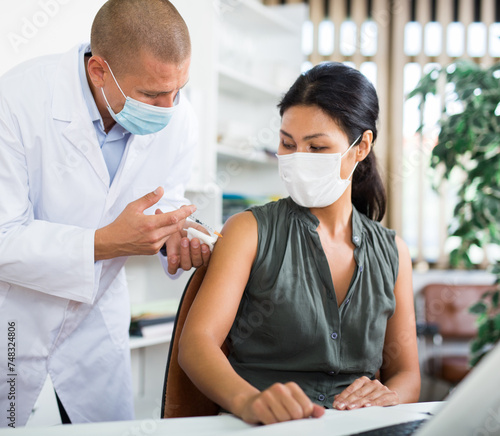 Doctor in a protective face mask giving coronavirus vaccine to pacient in modern office