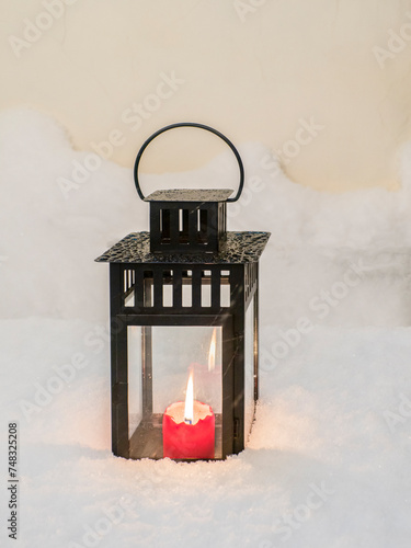 Burning red Christmas candle on fresh snow background,  lantern in snow on the table snow covered