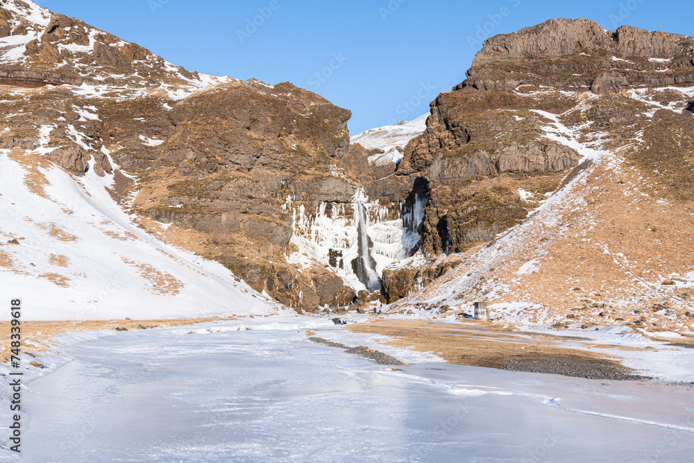 Beautiful winter view of the Icelandic Írárfoss waterfall in the south of Iceland between towns Hvolsvöllur and Vík with some tourists. Amazing frozen waterfall coming from a volcanic cliff in Iceland