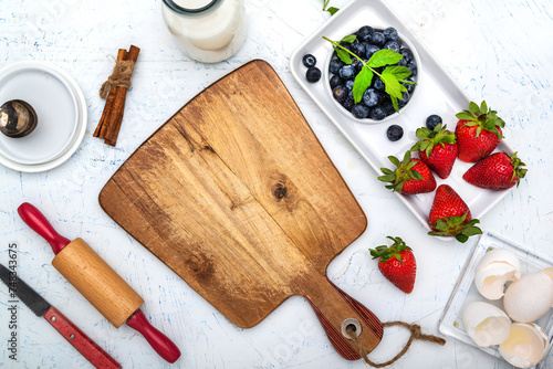 Cutting board, berries and ingredients for making pie with berries on a wooden table. Space for text.
