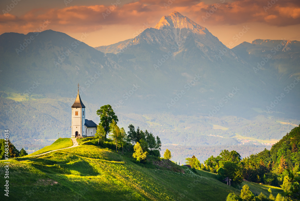Jamnik, Slovenia - Aerial view of the beautiful hilltop church, amazing golden sunset over Kamnik–Savinja Alps, Skofja Loka