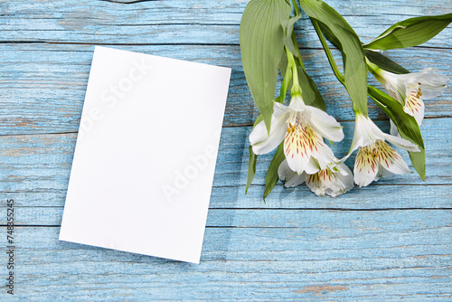 White blank card mockup and alstroemeria flowers on blue wood background, top view, flat lay photo