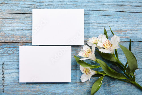 Two blank white cards on a rustic blue wooden surface, accompanied by white flowers, top view, flat lay