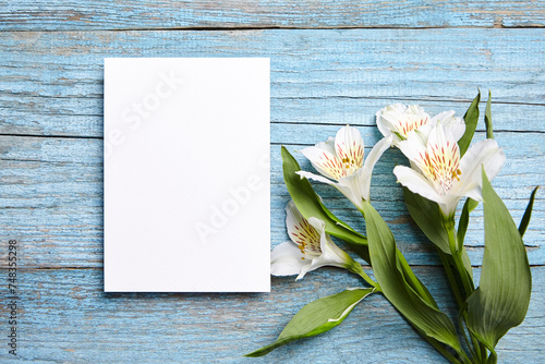 White blank card mockup and alstroemeria flowers on blue wood background, top view, flat lay