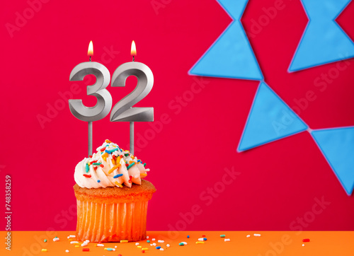 Number 32 candle with birthday cupcake on a red background with blue pennants