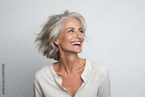 Portrait of a happy mature woman laughing and looking up against grey background