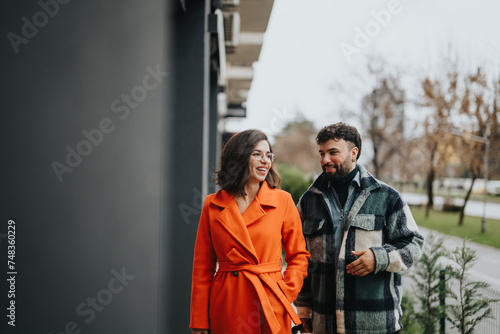 A fashion-forward couple walks together with smiles, enjoying an outdoor autumn day in an urban park environment.
