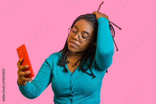 retrato de una mujer afro latina usando su móvil para hacerse un selfie mientras se lleva una mano al pelo photo