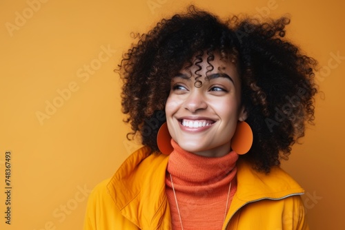 Cheerful young african american woman with afro hairstyle and orange turtleneck on yellow background © Inigo