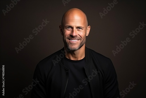 Portrait of a handsome bald man smiling at the camera on a dark background