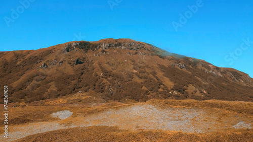 Colorful autumn vegetation in a mountainous area. Clip. A sunny day, blue sky and golden hills.