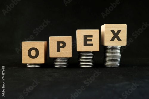 Increase in opex or operational expenses concept. Wooden blocks with increasing stack of coins in black background. photo