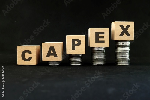 Obraz na płótnie Increase in capex or capital expenditure concept. Wooden blocks with increasing stack of coins in black background. w salonie