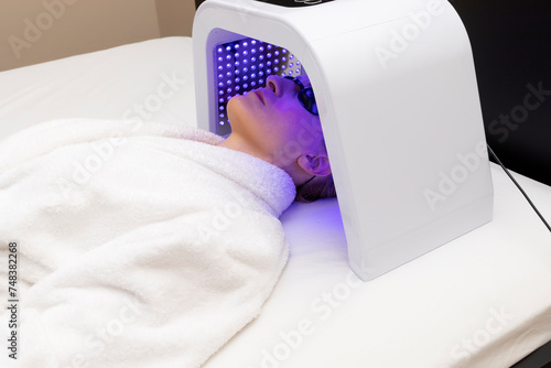 Home Skin Care Procedure. Cosmetic Led Light Face Mask. Woman In Her 30s Lying Under Facial Regenerative Treatment Mask On Bed In Bedroom. Acne, Spot Cure. Beauty Photon Therapy. Horizontal Plane