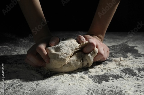 Making bread. Woman kneading dough at table on dark background, closeup