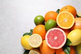 Pile of different fresh citrus fruits and leaves on grey textured table, flat lay. Space for text