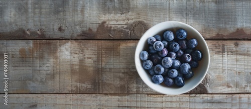 A white bowl filled with fresh ripe blueberries sits on top of a wooden table in this straightforward and unembellished still life.