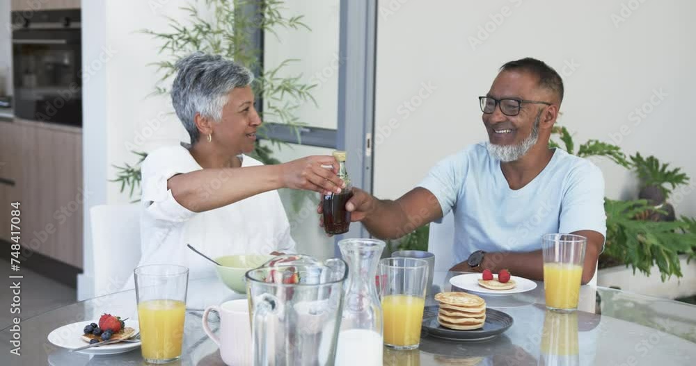 Biracial couple enjoys a hearty breakfast, the man opening a bottle of champagne Biracial couple enjoys a hearty breakfast, the man opening a bottle of champagne