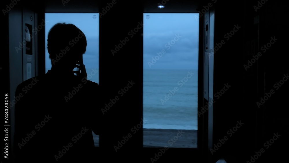 Young tourist with a smartphone looks out of the window of a moving train. Stock clip. Rear view of a male silhouette talking on phone in train.
