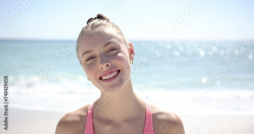 Wallpaper Mural A young Caucasian woman with blonde hair, wearing a casual pink top, smiles brightly at the beach Torontodigital.ca