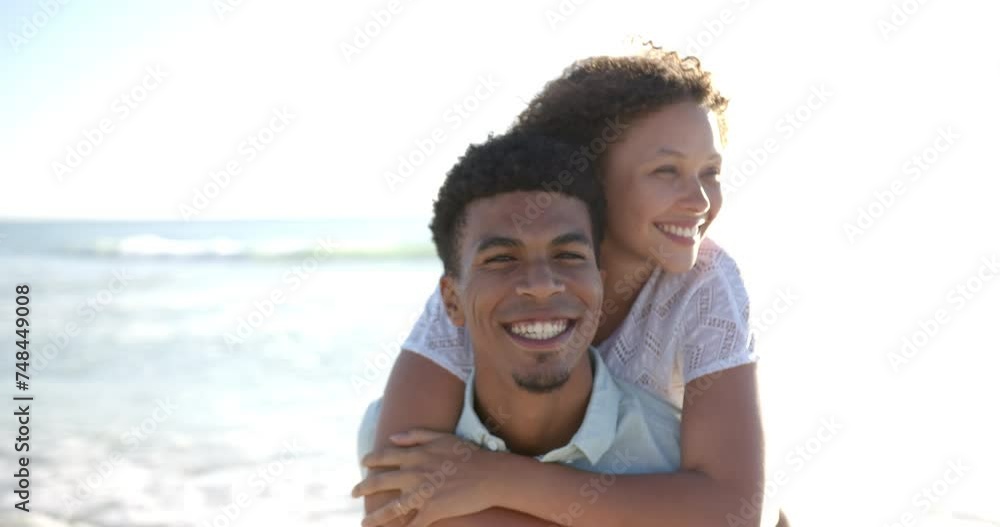Biracial couple embraces on a sunny beach, with the woman's arms wrapped around the man's shoulders Biracial couple embraces on a sunny beach, with the woman's arms wrapped around the man's shoulders
