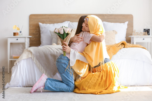 Little girl and her Muslim mom with tulips hugging in bedroom on Mother's Day photo