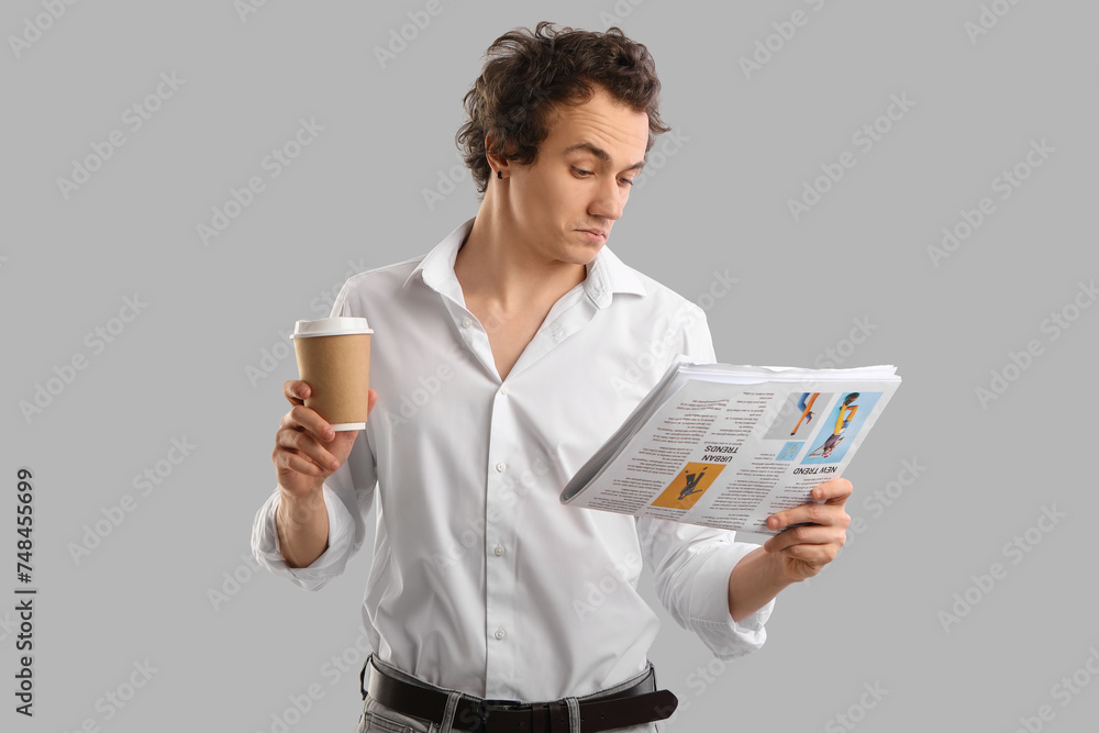 Young man with cup of coffee reading newspaper on grey background Young man with cup of coffee reading newspaper on grey background