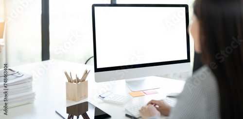 Rear view of woman using desktop computer while sitting at office, mockup blank screen monitor of graphic design. © NAMPIX