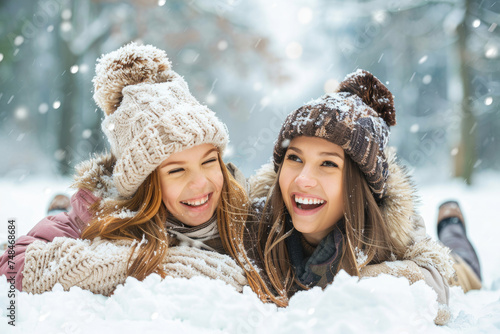 Cheerful mother and daughter having fun laying in snow outdoors