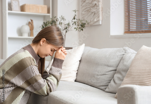 Young woman praying near sofa at home