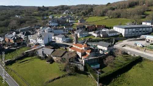 Aerial orbit around lush green valley and historic church of San Xoan de Rio at midday photo