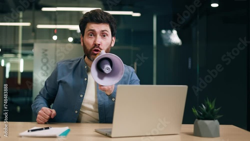 Bossy entrepreneur in casual outfit expressing negative emotions while yelling through bullhorn in workspace with pc. Cynical chef showing disrespect for employees at company office with glassy walls. photo