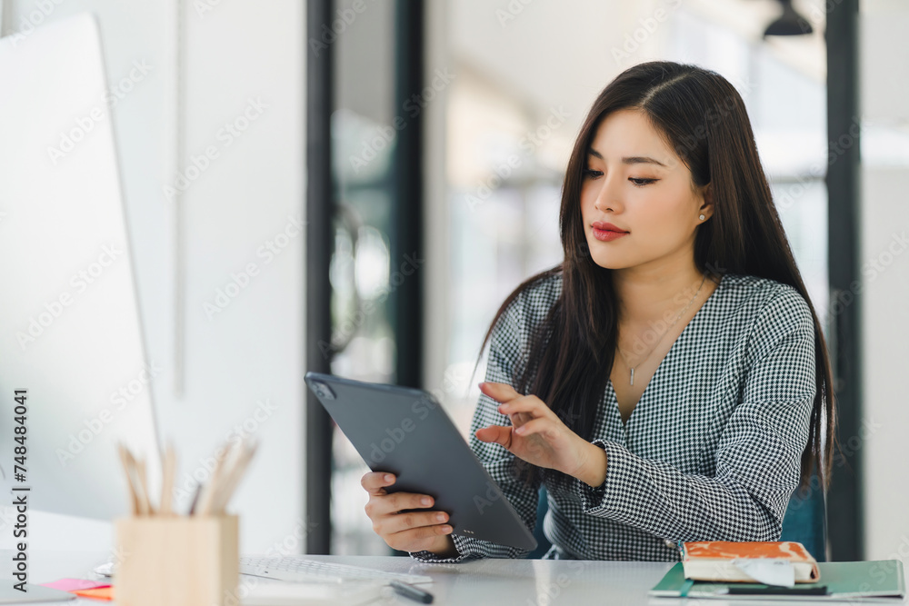 Asian professional businesswoman working on a tablet and desktop computer in a corporate office. Asian professional businesswoman working on a tablet and desktop computer in a corporate office.