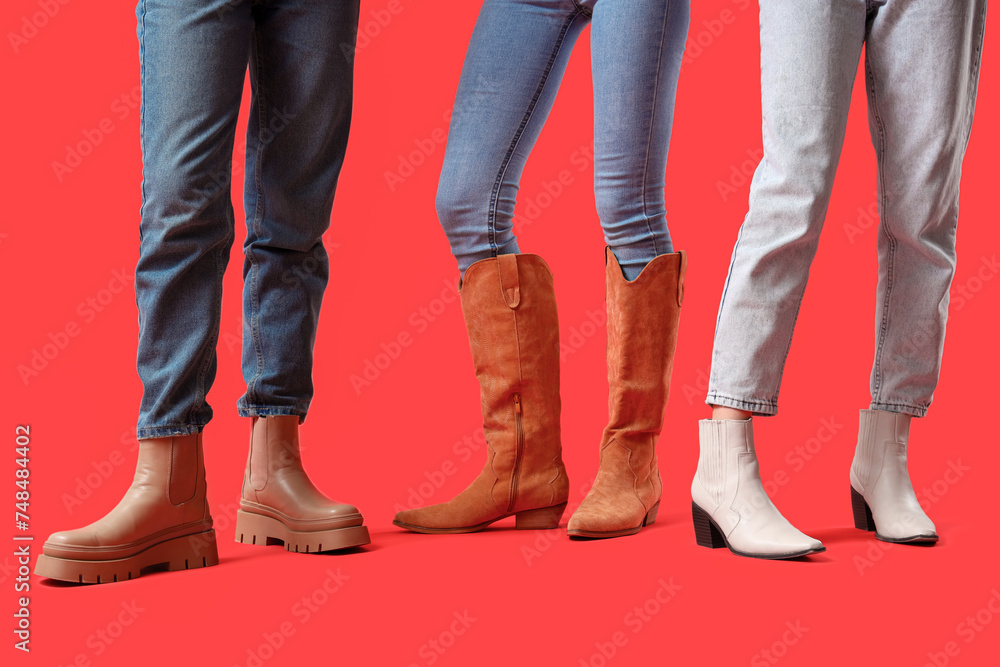 Female legs wearing different boots on red background