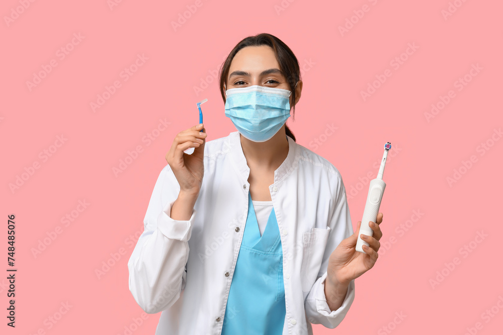 Young female dentist in mask with electric toothbrush and brush for cleaning braces on pink background Young female dentist in mask with electric toothbrush and brush for cleaning braces on pink background