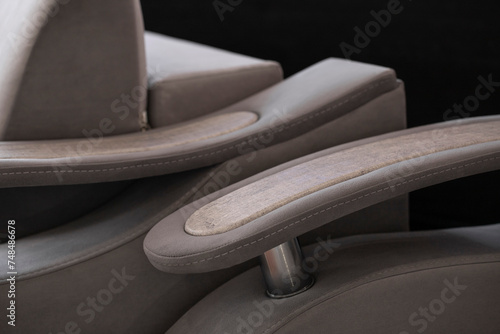 Designer curved armrests in the shape of a wave with a wooden element on a chrome-plated tube. Comfortable upholstered furniture in retro style in gray shades and close-up embroidery.