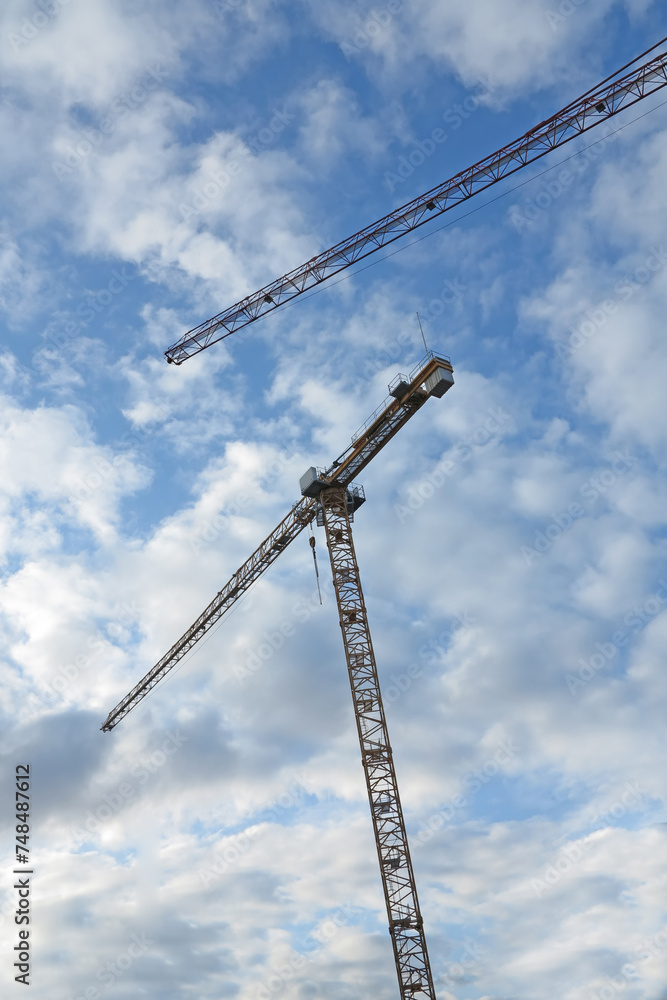 Crane, construction and clouds or blue sky background for building with heavy machinery or material outdoor. Hoist in city, urban or industrial development with low angle, tools or overhead equipment Crane, construction and clouds or blue sky background for building with heavy machinery or material outdoor. Hoist in city, urban or industrial development with low angle, tools or overhead equipment