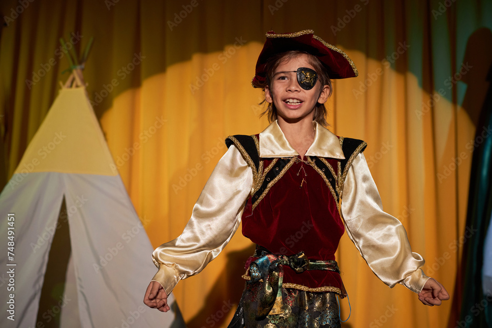 Naklejka premium Waist up portrait of young boy wearing pirate costume performing on stage in school play