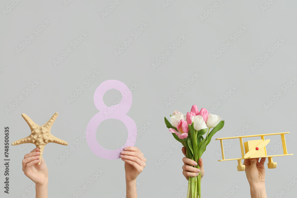 Female hands with paper figure 8, toy plane and tulip flowers for International Women's Day on grey background