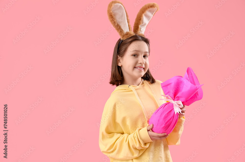 Cute little girl with Easter bunny ears and gift on pink background