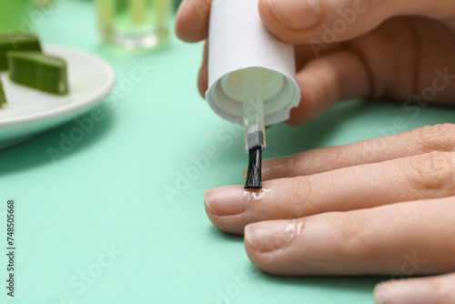 Woman applying cuticle oil onto fingernails on turquoise background  closeup