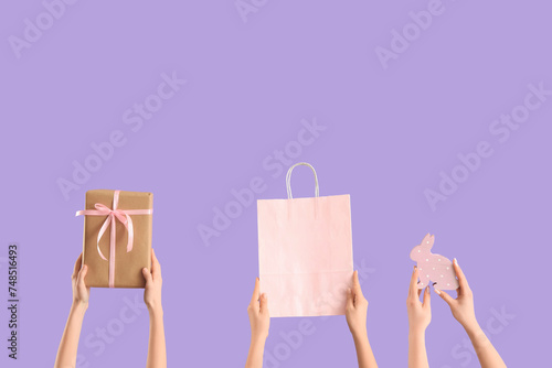 Women with shopping bag, gift and decor on lilac background. Easter Sale