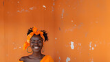 jeune et belle femme à la peau noire, d'origine antillaise, africaine, des caraïbes ou de l'océan indien,  souriante devant un mur orange assorti à sa tenue elle aussi orange. Fond avec copyspace