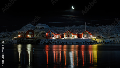 Waxing Crescent Moon above the little snow covered island and the cabins on it. Lofoten, Northern Norway.. 
