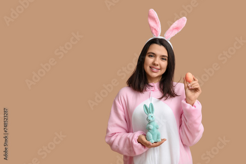 Beautiful young woman in bunny costume with Easter egg and rabbit on brown background