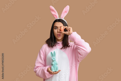 Beautiful young woman in bunny costume with Easter egg and rabbit on brown background